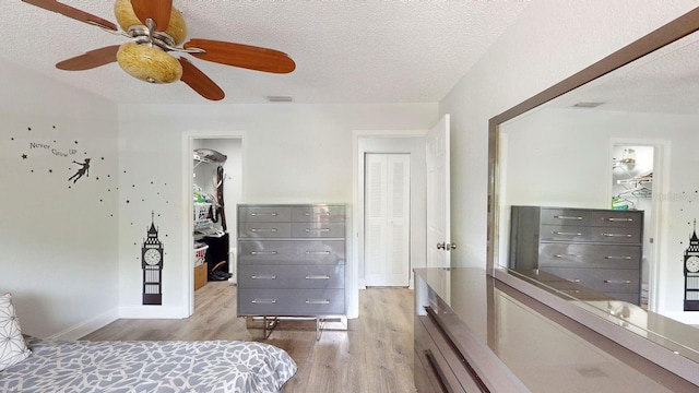 bedroom with a walk in closet, ceiling fan, a textured ceiling, a closet, and light wood-type flooring