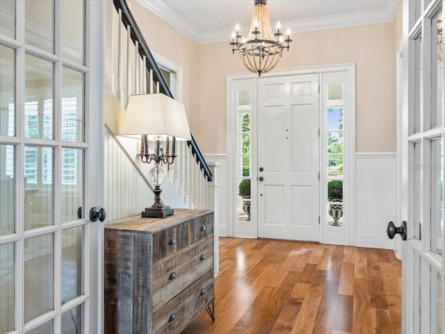 foyer featuring an inviting chandelier, ornamental molding, a wealth of natural light, and light hardwood / wood-style flooring