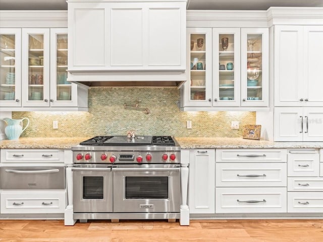 kitchen with wall chimney range hood, light hardwood / wood-style flooring, white cabinets, range with two ovens, and light stone counters