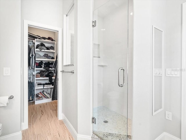 bathroom with an enclosed shower, toilet, and wood-type flooring