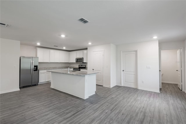 kitchen with appliances with stainless steel finishes, light stone counters, white cabinets, light hardwood / wood-style flooring, and a kitchen island with sink