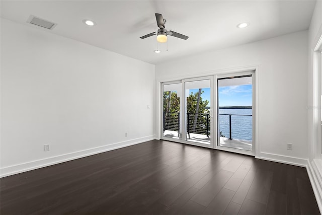 empty room featuring dark wood-type flooring, a water view, and ceiling fan