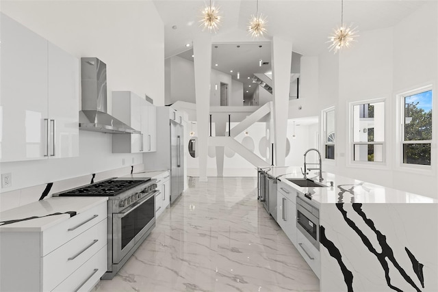 kitchen with decorative light fixtures, stainless steel appliances, sink, wall chimney exhaust hood, and a towering ceiling