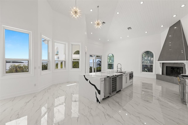 kitchen featuring high vaulted ceiling, a notable chandelier, a tile fireplace, sink, and an island with sink