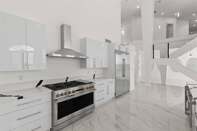 kitchen with wall chimney range hood, white cabinets, high quality appliances, and a towering ceiling