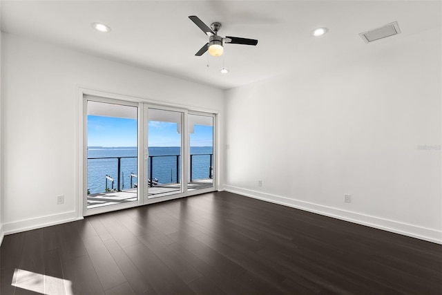 unfurnished room featuring plenty of natural light, ceiling fan, a water view, and dark wood-type flooring