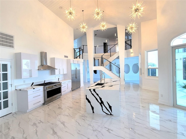 kitchen featuring decorative light fixtures, high vaulted ceiling, white cabinetry, wall chimney range hood, and premium appliances