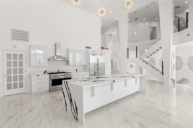 kitchen with high end appliances, high vaulted ceiling, white cabinets, and wall chimney range hood