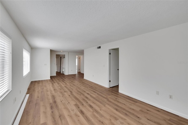 unfurnished room featuring baseboard heating, a textured ceiling, and light wood-type flooring