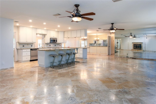 kitchen featuring ceiling fan with notable chandelier, a kitchen island, pendant lighting, white cabinets, and appliances with stainless steel finishes