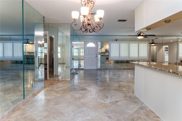 kitchen with ceiling fan with notable chandelier, light stone counters, decorative light fixtures, and light tile floors