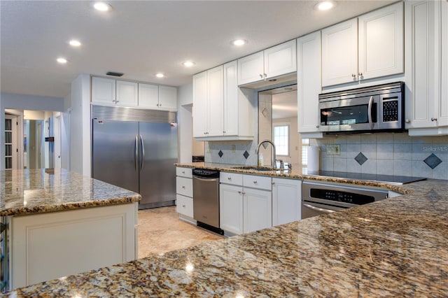 kitchen with stainless steel appliances, dark stone countertops, white cabinets, and backsplash