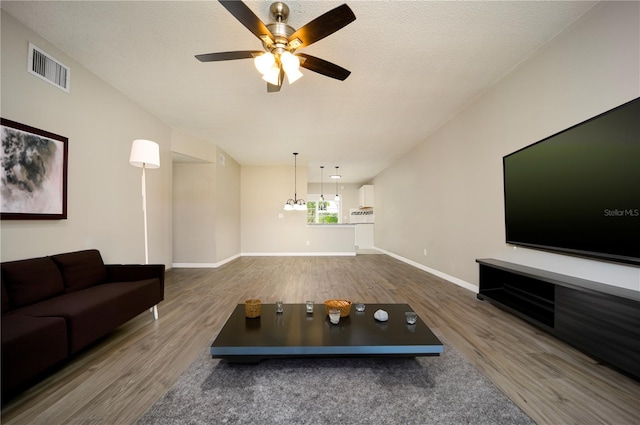 living room with a textured ceiling, wood-type flooring, and ceiling fan with notable chandelier