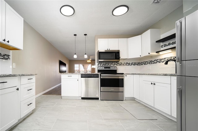 kitchen with backsplash, appliances with stainless steel finishes, white cabinets, light stone counters, and pendant lighting