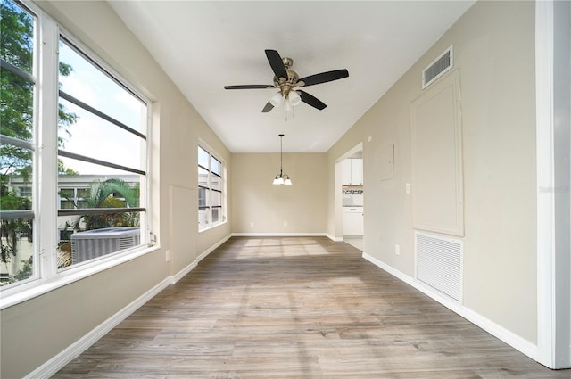 unfurnished room featuring ceiling fan with notable chandelier and light wood-type flooring