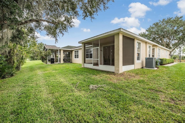 back of property with central AC unit, a sunroom, and a lawn