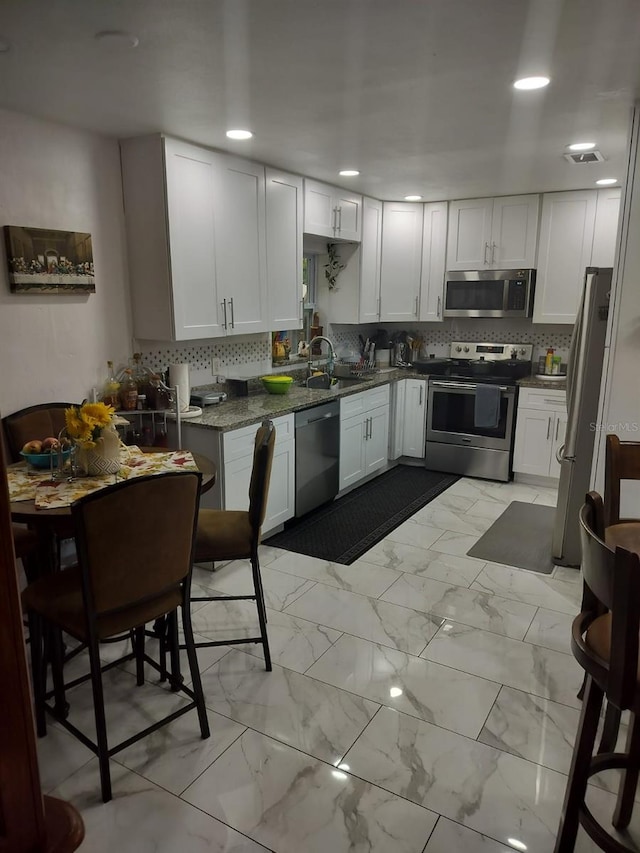 kitchen with white cabinetry, backsplash, stainless steel appliances, light tile floors, and dark stone counters