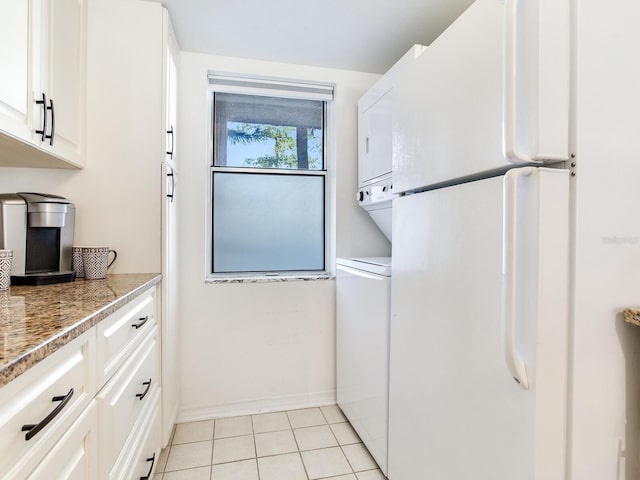 kitchen featuring stacked washer and dryer, white cabinetry, freestanding refrigerator, light tile patterned floors, and baseboards