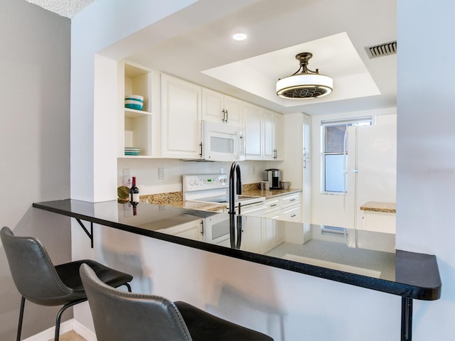 kitchen featuring a kitchen breakfast bar, kitchen peninsula, white cabinetry, and white appliances