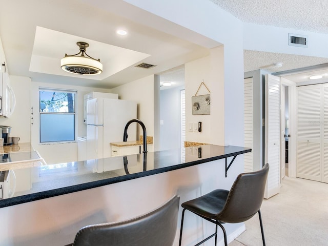 kitchen featuring kitchen peninsula, light colored carpet, a raised ceiling, and white appliances