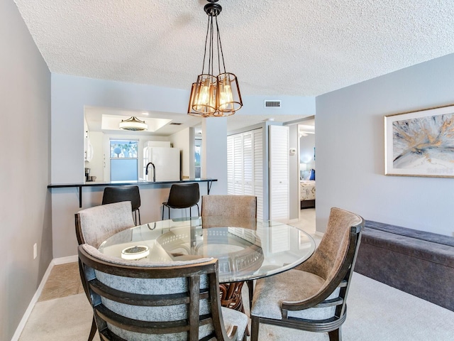 dining room featuring visible vents, light colored carpet, a textured ceiling, and baseboards