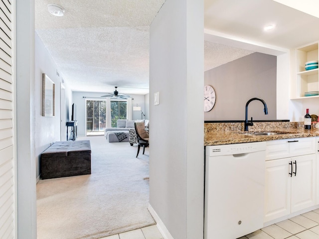 kitchen with white cabinets, white dishwasher, dark stone countertops, sink, and light colored carpet