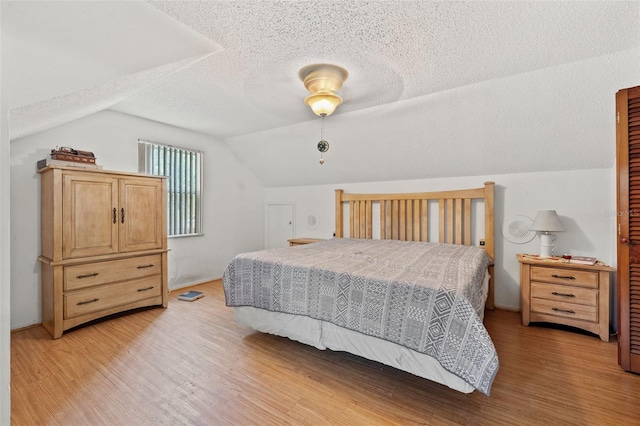 bedroom featuring a textured ceiling, vaulted ceiling, and light hardwood / wood-style flooring