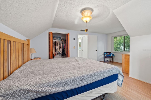 bedroom with a closet, a walk in closet, light hardwood / wood-style flooring, a textured ceiling, and vaulted ceiling