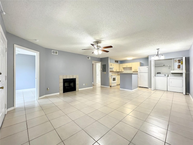 unfurnished living room with washing machine and dryer, ceiling fan with notable chandelier, light tile flooring, a fireplace, and a textured ceiling