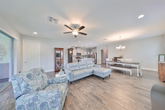 living room with ceiling fan with notable chandelier and light hardwood / wood-style floors