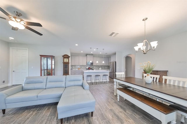 living room with ceiling fan with notable chandelier and wood-type flooring