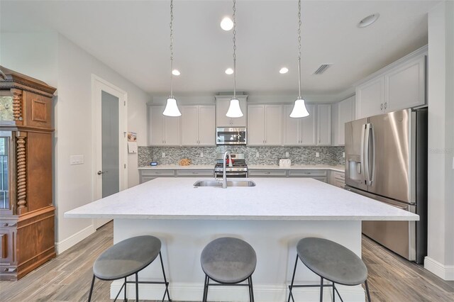 kitchen featuring decorative light fixtures, tasteful backsplash, stainless steel appliances, a center island with sink, and light hardwood / wood-style floors