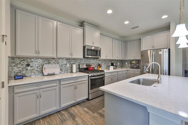 kitchen featuring stainless steel appliances, hanging light fixtures, dark hardwood / wood-style flooring, sink, and backsplash