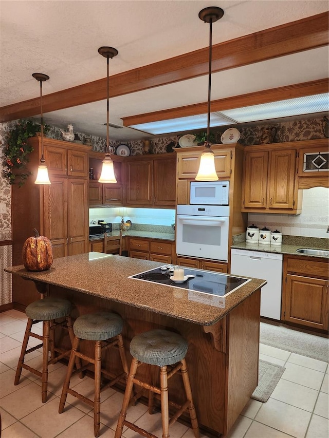 kitchen featuring hanging light fixtures, white appliances, light tile floors, a kitchen island, and a breakfast bar area