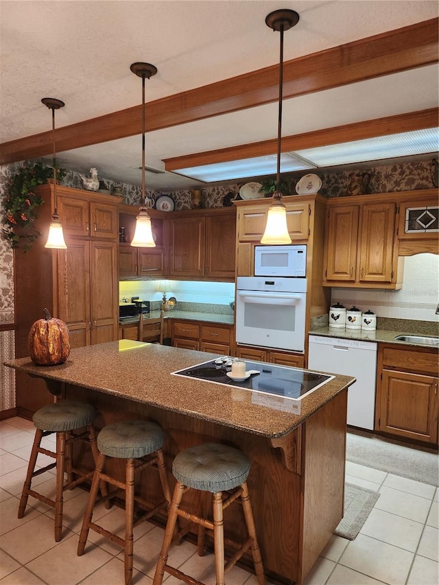 kitchen with pendant lighting, light tile floors, a kitchen island, white appliances, and a breakfast bar area