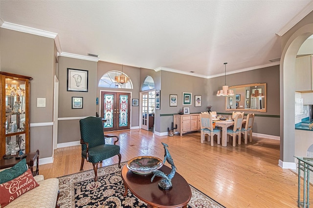 living room featuring crown molding, french doors, a notable chandelier, and light wood-type flooring