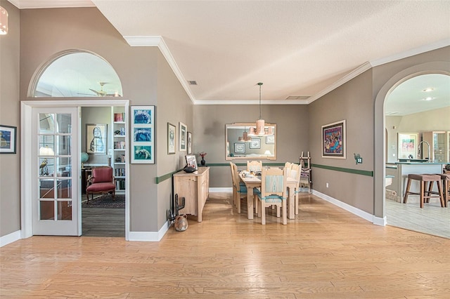 dining room with lofted ceiling, light wood-type flooring, crown molding, and french doors