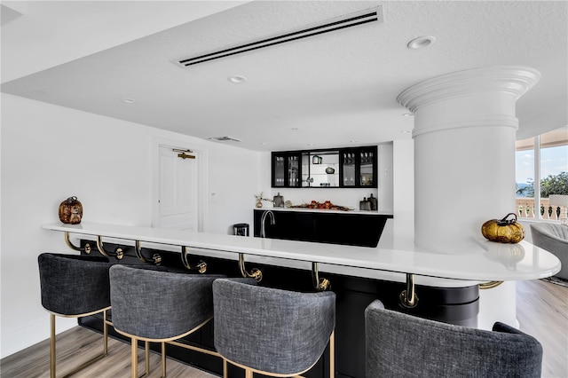 bar featuring light wood-type flooring, a textured ceiling, and ornate columns