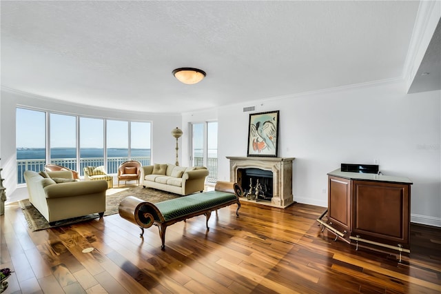 living room with a textured ceiling, a water view, dark hardwood / wood-style flooring, and ornamental molding