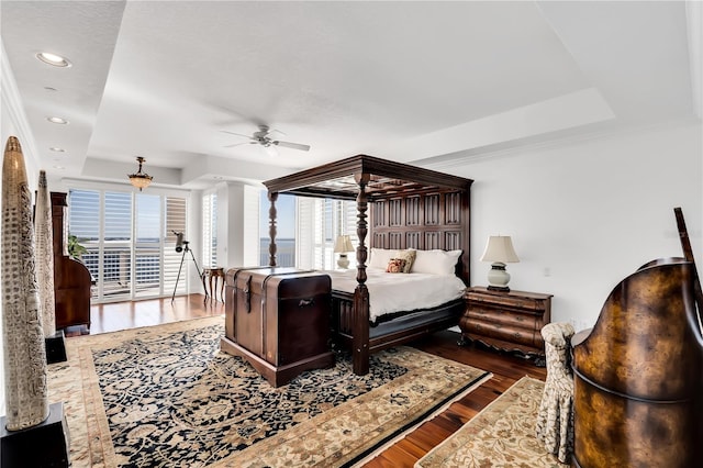 bedroom with ceiling fan, wood-type flooring, multiple windows, and a raised ceiling