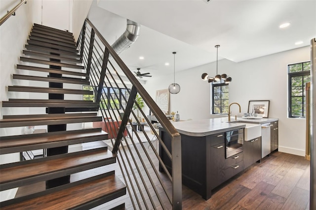 interior space with dark hardwood / wood-style floors, an island with sink, sink, pendant lighting, and ceiling fan with notable chandelier