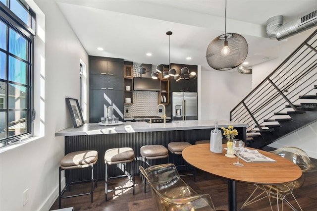 bar with wall chimney range hood, tasteful backsplash, dark hardwood / wood-style floors, stainless steel refrigerator with ice dispenser, and decorative light fixtures