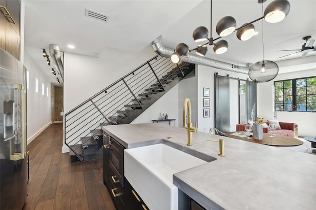 kitchen featuring stainless steel fridge with ice dispenser, dark hardwood / wood-style flooring, a barn door, pendant lighting, and sink