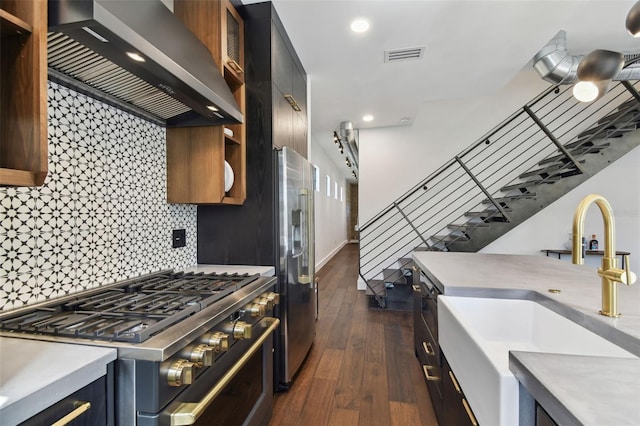 kitchen with wall chimney range hood, decorative backsplash, dark wood-type flooring, sink, and premium appliances