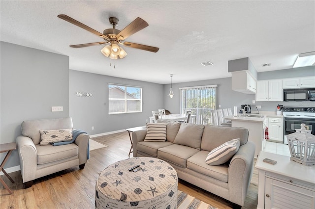 living room with ceiling fan, sink, a textured ceiling, and light wood-type flooring