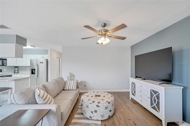 living room with ceiling fan, a textured ceiling, and light wood-type flooring