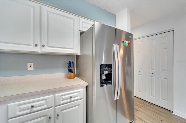 kitchen featuring white cabinets, a textured ceiling, stainless steel fridge, and light hardwood / wood-style floors