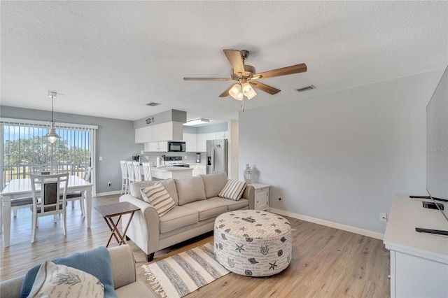 living room featuring ceiling fan, light hardwood / wood-style floors, and a textured ceiling