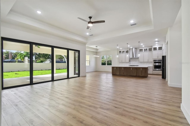 unfurnished living room with ceiling fan, a tray ceiling, and light hardwood / wood-style floors