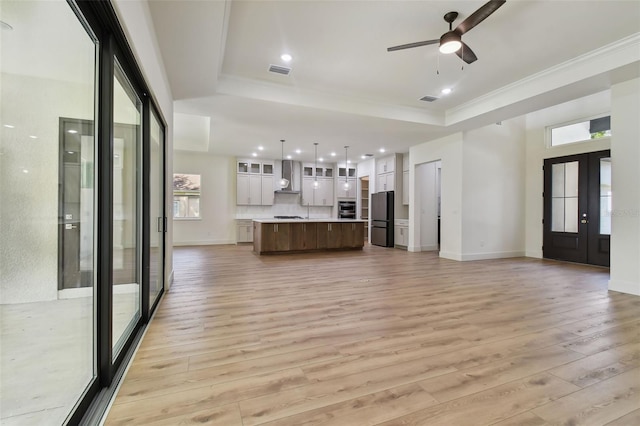 unfurnished living room with french doors, a raised ceiling, light hardwood / wood-style floors, and ceiling fan